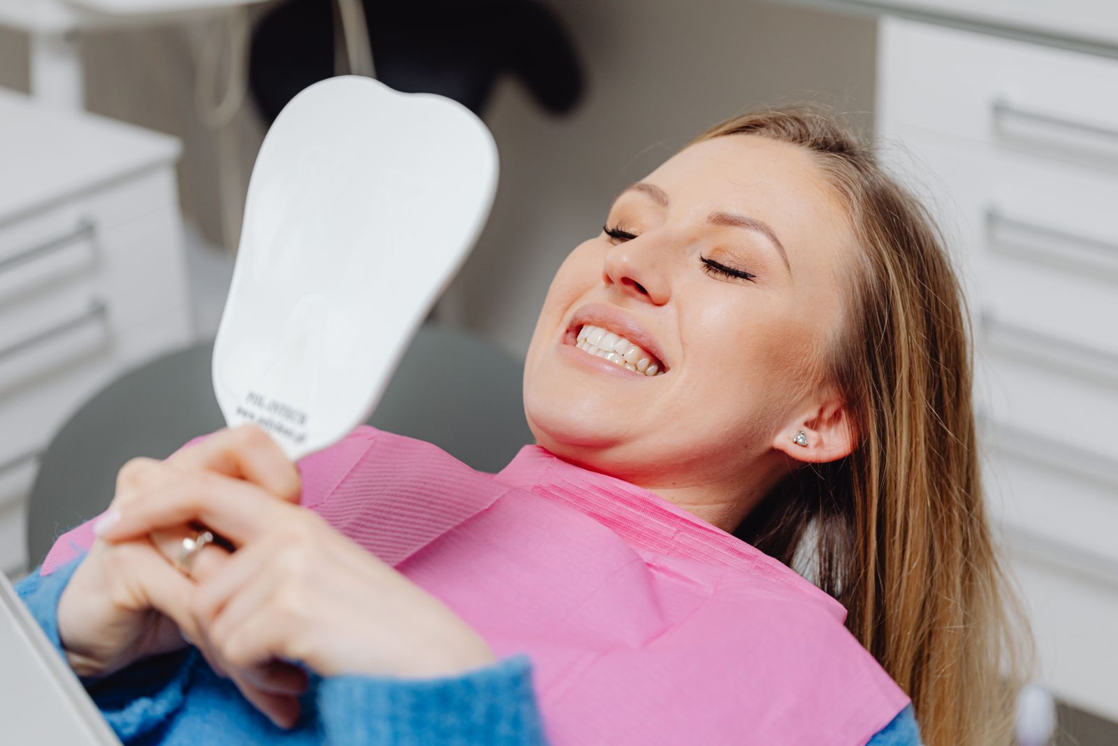 Paciente sonriendo mientras mira su sonrisa en un espejo durante su cita dental